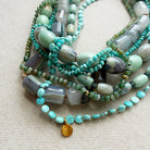 Multistrand beaded necklace with turquoise and green beads on a beige fabric background
