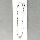 A multi-color sapphire necklace with a central imperial topaz pendant, displayed on a white background over a gray textured fabric background.