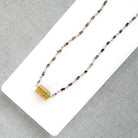 A multi-color sapphire necklace with a central imperial topaz pendant, displayed on a white background over a gray textured fabric background.