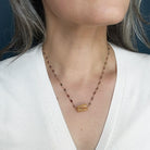 A close-up of a person wearing a multi-color sapphire necklace with a central imperial topaz pendant, paired with a white V-neck top.