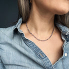 Person wearing a delicate iolite gemstone necklace with a dark background