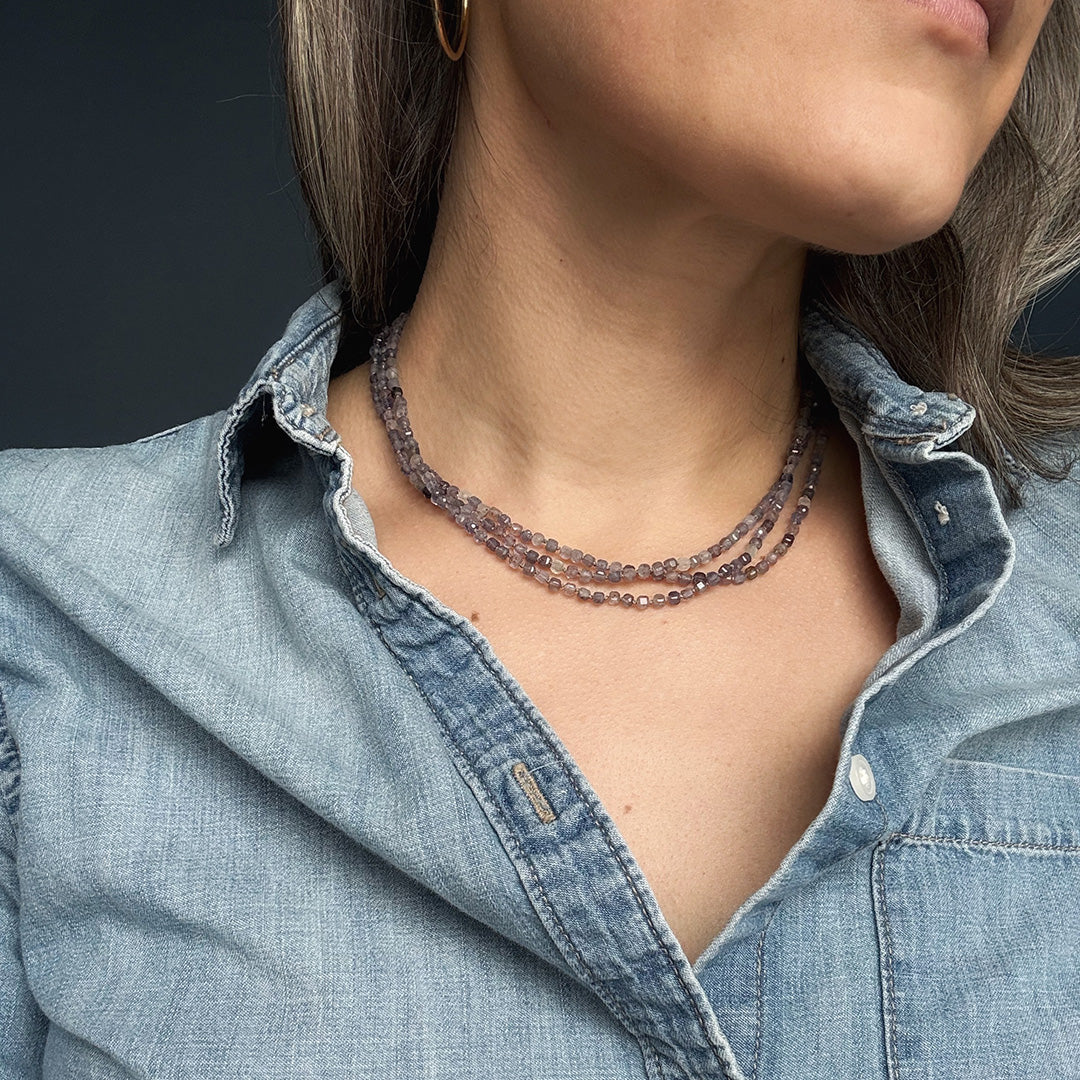 Person wearing a delicate iolite gemstone necklace with a dark background