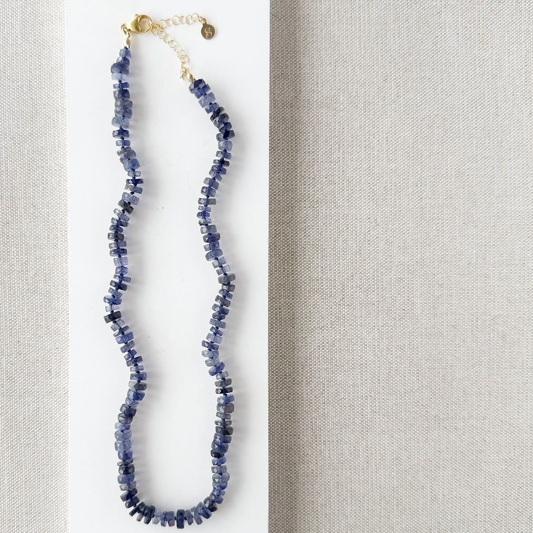 Iolite gemstone necklace on a white dish with a beige fabric background