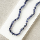 Iolite gemstone necklace on a white dish with a beige fabric background