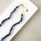 Iolite gemstone necklace on a white dish with a beige fabric background