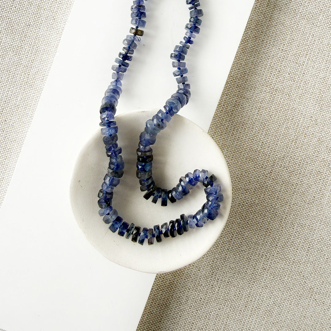 Iolite gemstone necklace on a white dish with a beige fabric background