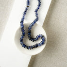 Iolite gemstone necklace on a white dish with a beige fabric background