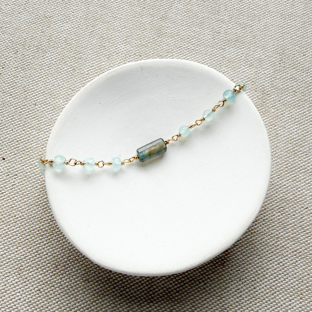 Bracelet with aqua chalcedony gemstones on a white dish against a beige background