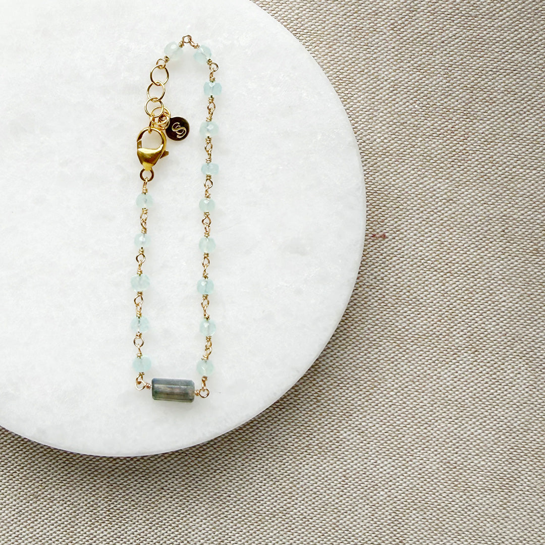 Gold bracelet with aqua chalcedony gemstones on a white marble surface