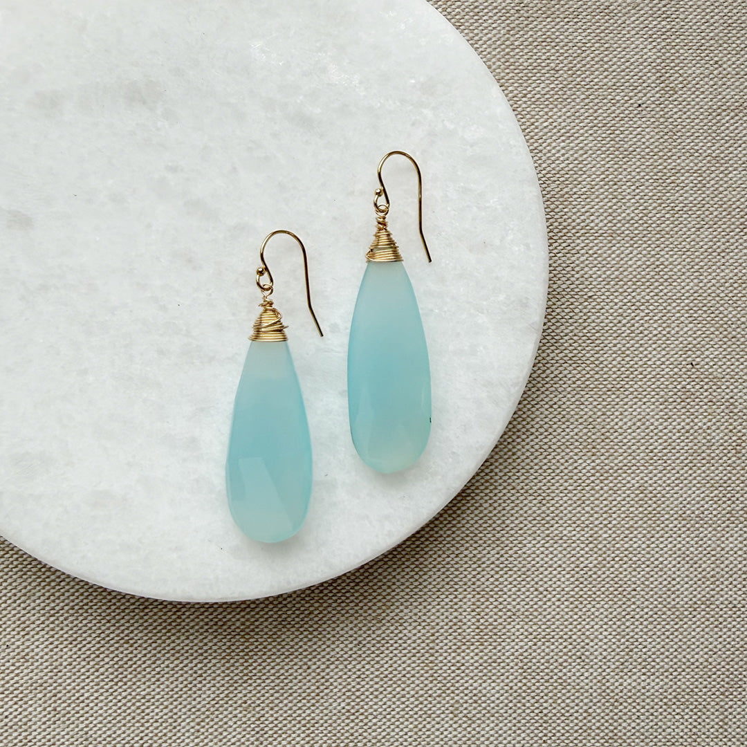 Pair of blue chalcedony teardrop earrings with gold hooks on a white plate.