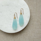 Pair of blue chalcedony teardrop earrings with gold hooks on a white plate.
