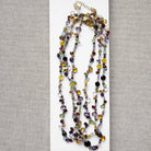 Multicolored gemstone necklaces on a white card with a gray background