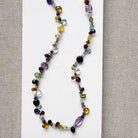 Multicolored gemstone necklace on a white card with a gray background