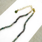 A necklace with small multicolored sapphire beads and a prominent oval pink sapphire at the center, displayed on a white ceramic dish against a light textured background.