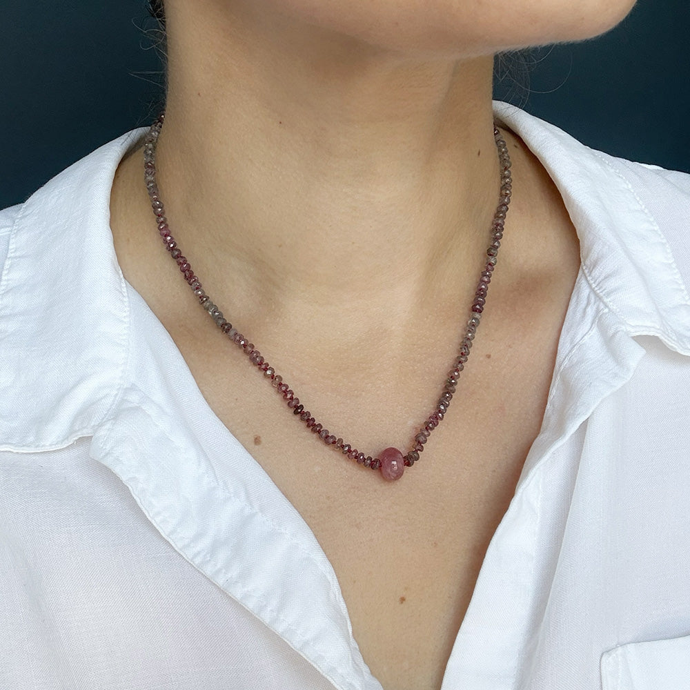 A close-up of a person wearing a sapphire with a single round sapphire in the center, styled with a white collared shirt.