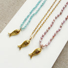 Three small gold fish charms, on gemstone and chain necklaces