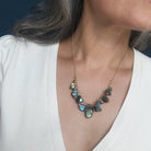 A close-up of a woman wearing a gold chain necklace with irregular, shimmering gray-green stones, paired with a white top.