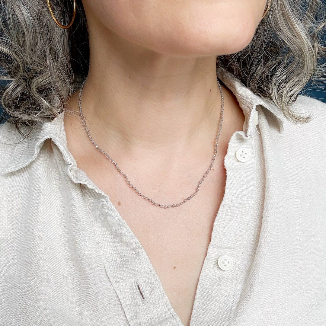 Person wearing necklace with small labradorite gemstones on a white background