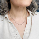 Person wearing necklace with small labradorite gemstones on a white background
