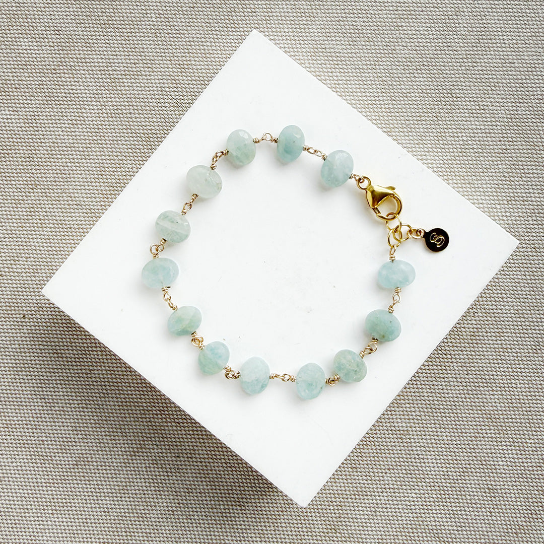 Aquamarine bracelet with gold clasp on a white card against a gray background