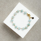 Aquamarine bracelet with gold clasp on a white card against a gray background
