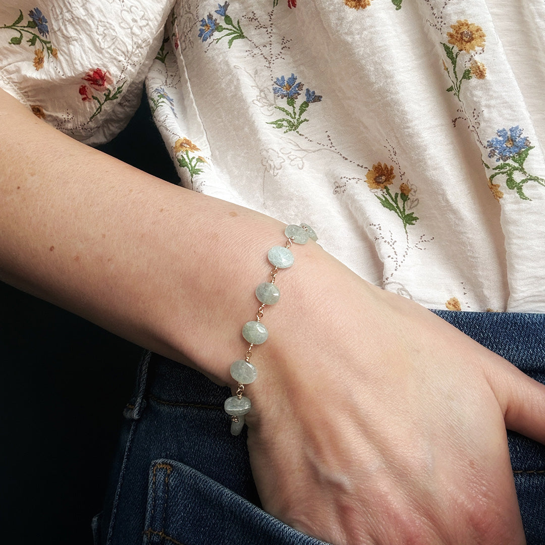 Close-up of a person's wrist wearing an aquamarine bracelet with a floral-patterned fabric background