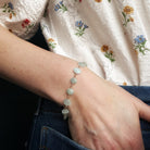 Close-up of a person's wrist wearing an aquamarine bracelet with a floral-patterned fabric background