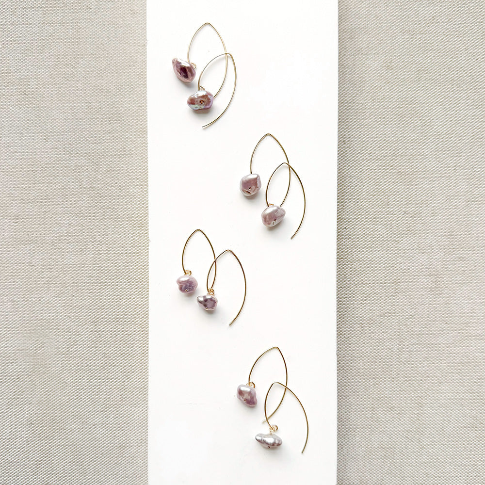 Irregular lavender pearl on a gold v-wire earring, displayed on a white card