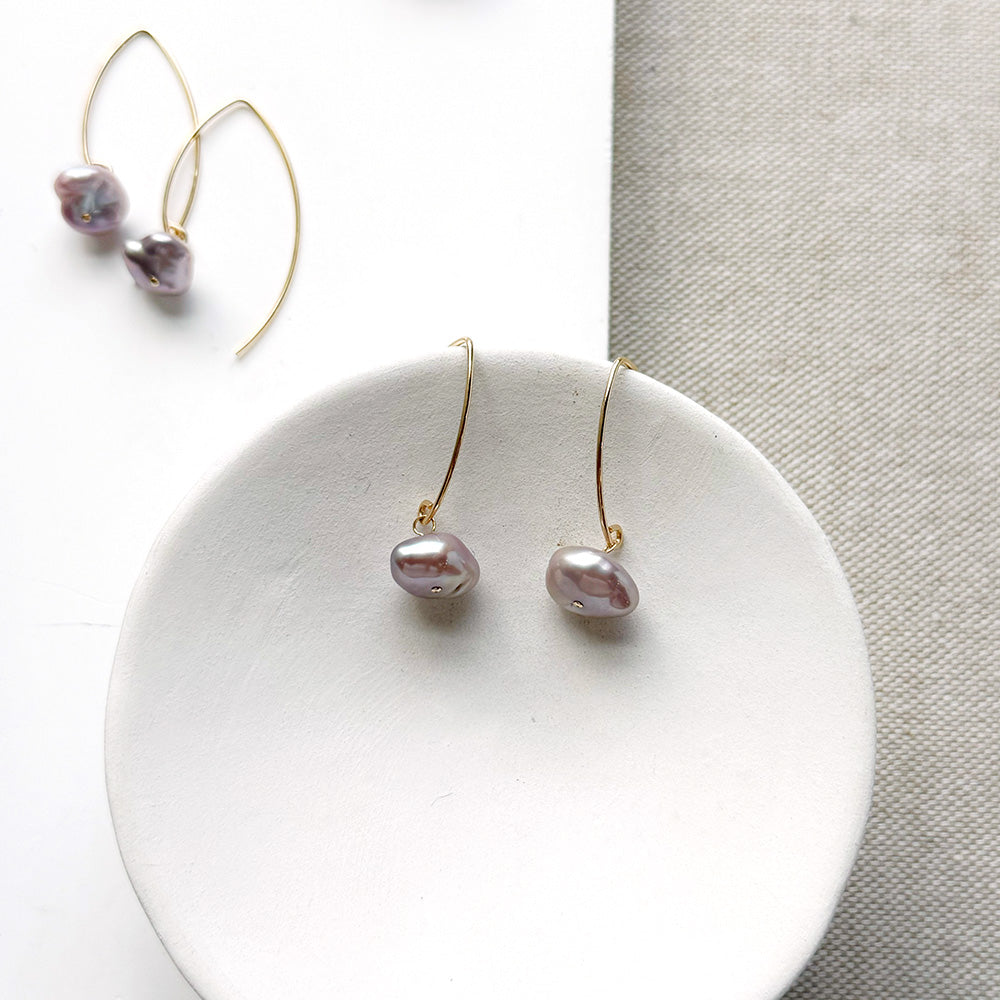 Irregular lavender pearl on a gold v-wire earring, displayed on a white card