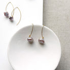 Irregular lavender pearl on a gold v-wire earring, displayed on a white card
