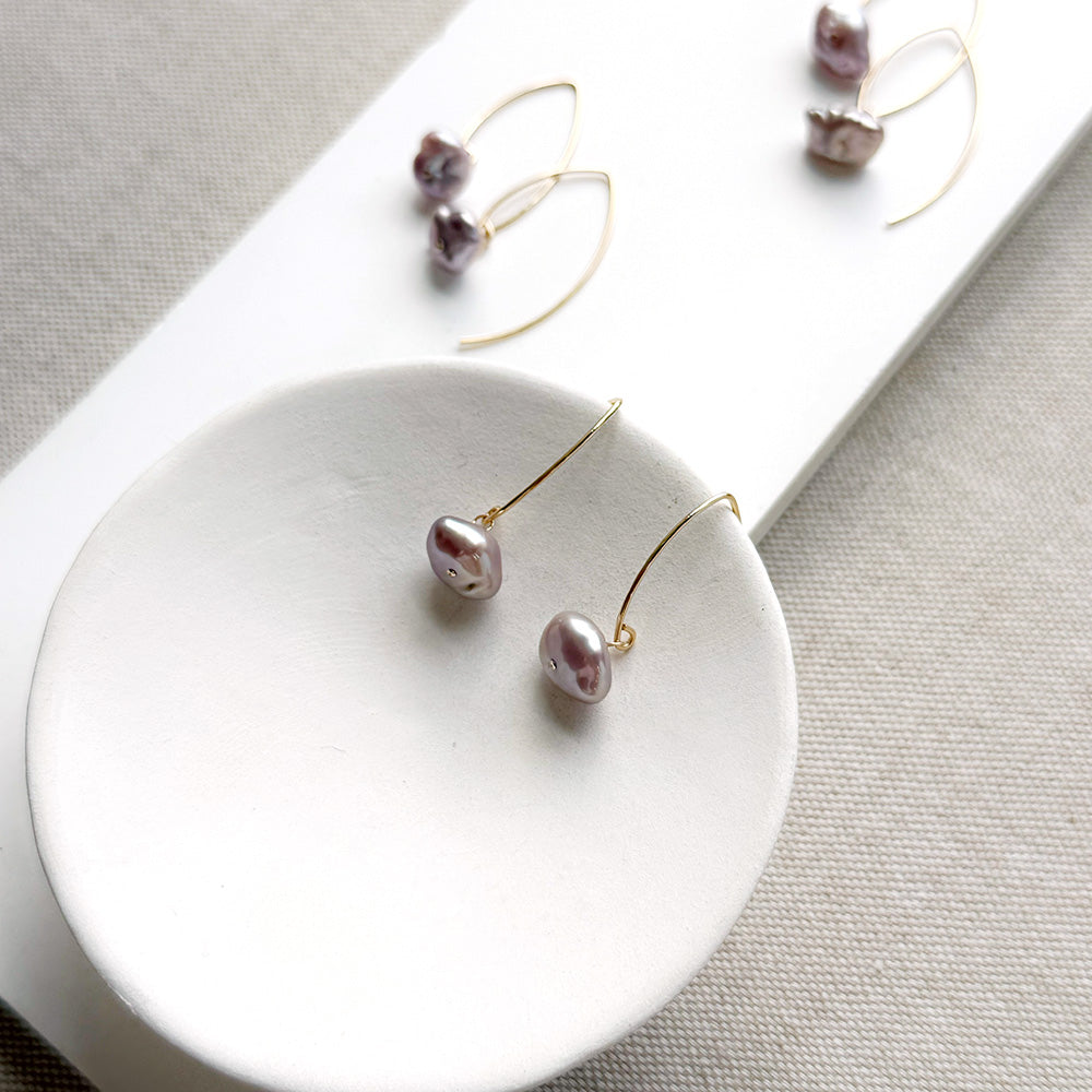 Irregular lavender pearl on a gold v-wire earring, displayed on a white card