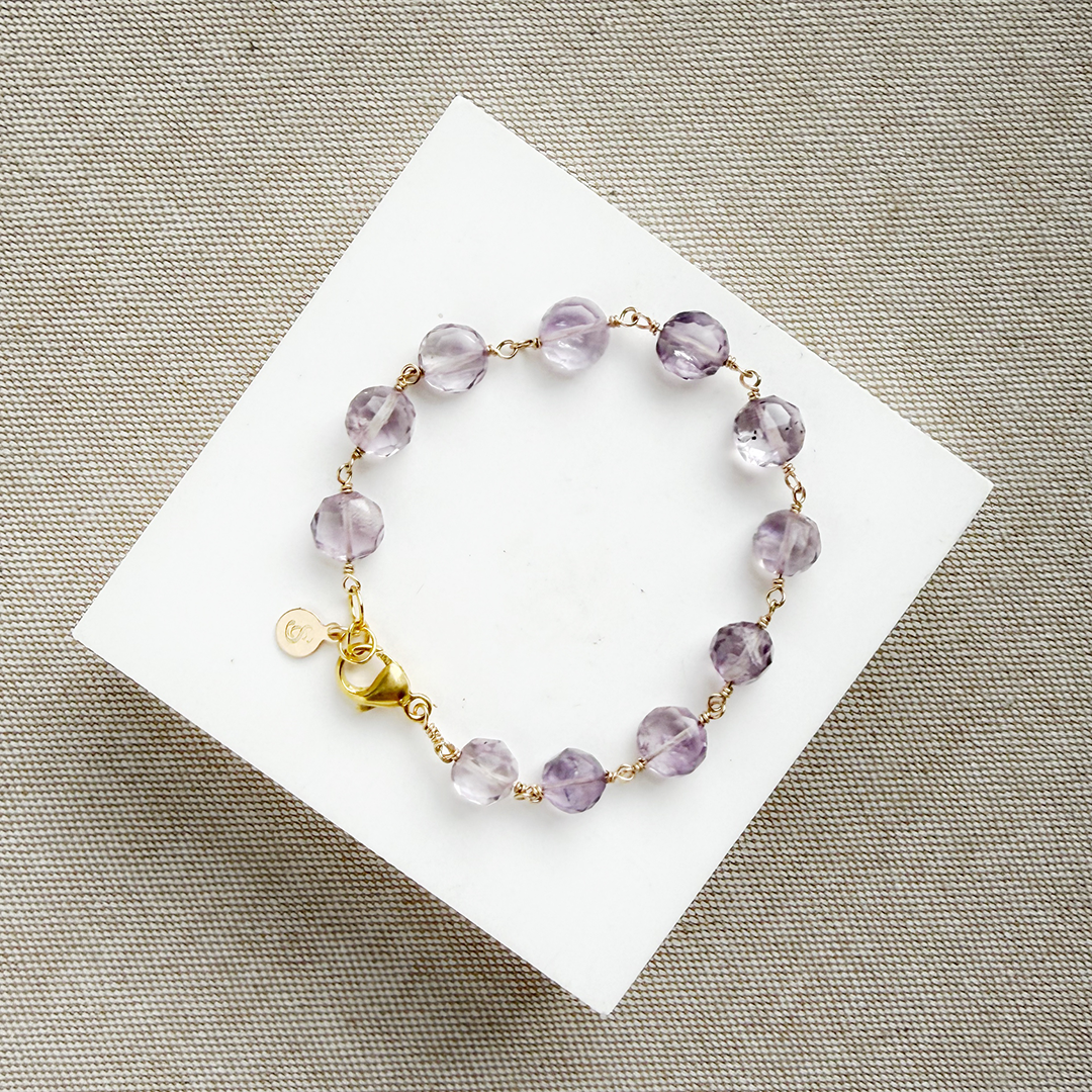 Amethyst bracelet with gold accents on a white card against a beige background