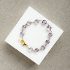 Amethyst bracelet with gold accents on a white card against a beige background