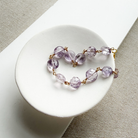 Amethyst bracelet with gold accents in a white dish against a beige background