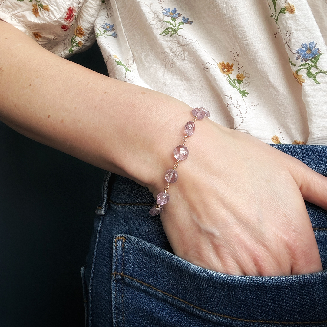 Person wearing a amethyst bracelet with against a floral shirt and denim jeans.