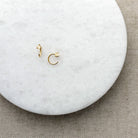 Two tiny gold reverse huggie style earring with opal stones on a round marble surface with a beige fabric background
