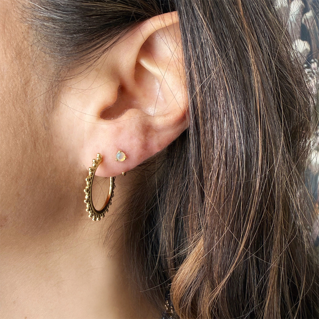 Close up of dark haired woman wearing a gold reverse huggie style earring with opal stone 