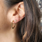 Close up of dark haired woman wearing a gold reverse huggie style earring with opal stone 