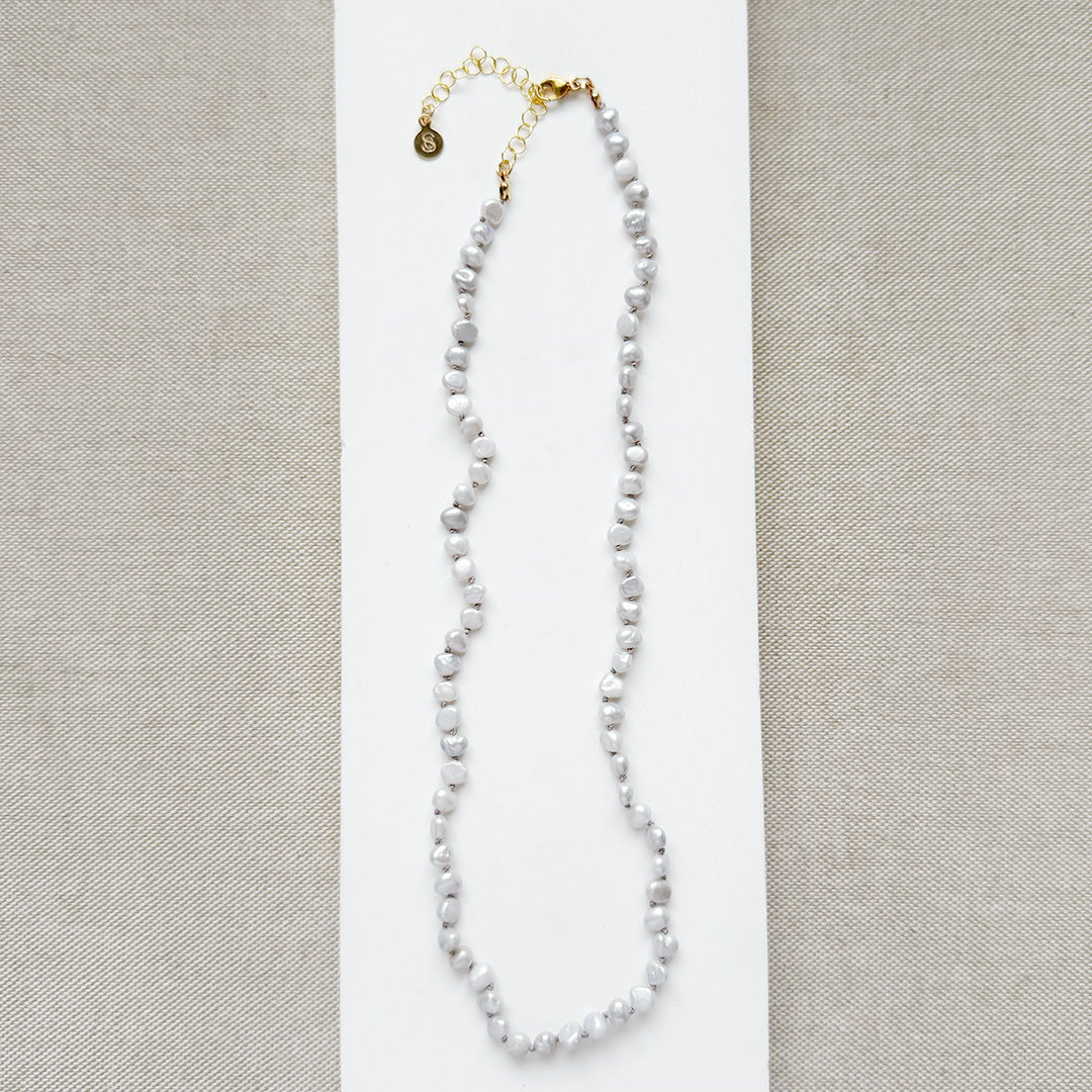 Pearl necklace with gold clasp on a light gray background