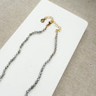 Clasp and extender for a small labradorite gems knotted necklace on a white surface with a beige background