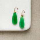Green chalcedony teardrop earrings with gold wire hooks on a white surface.