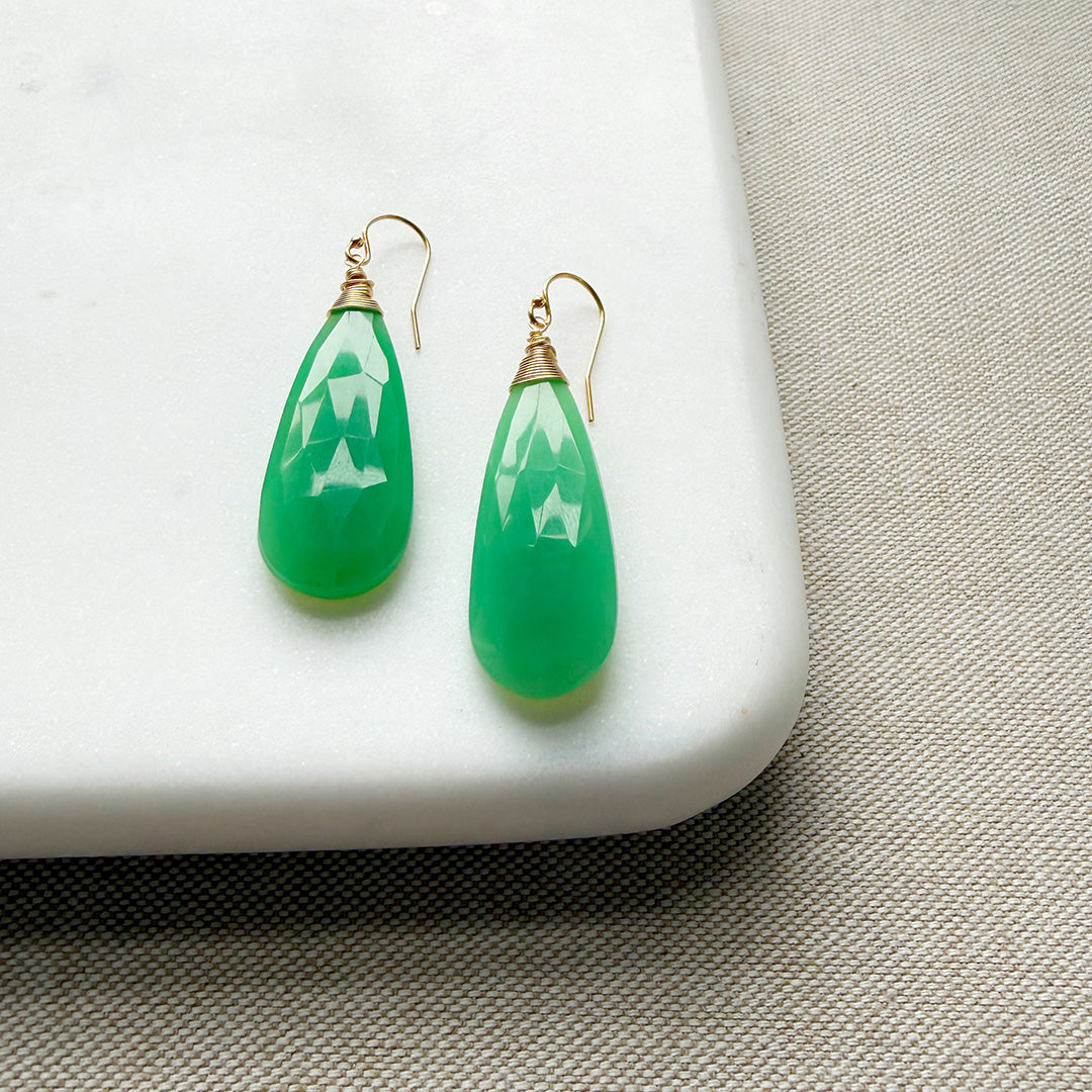 Green chalcedony teardrop earrings on a white platform with a beige fabric background