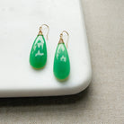 Green chalcedony teardrop earrings on a white platform with a beige fabric background