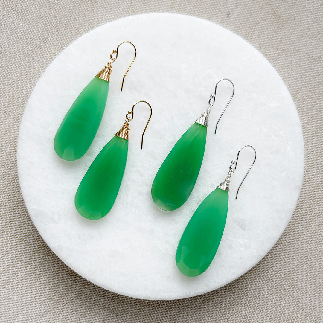 Green chalcedony teardrop earrings on a white circular stand with a beige background