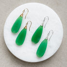 Green chalcedony teardrop earrings on a white circular stand with a beige background