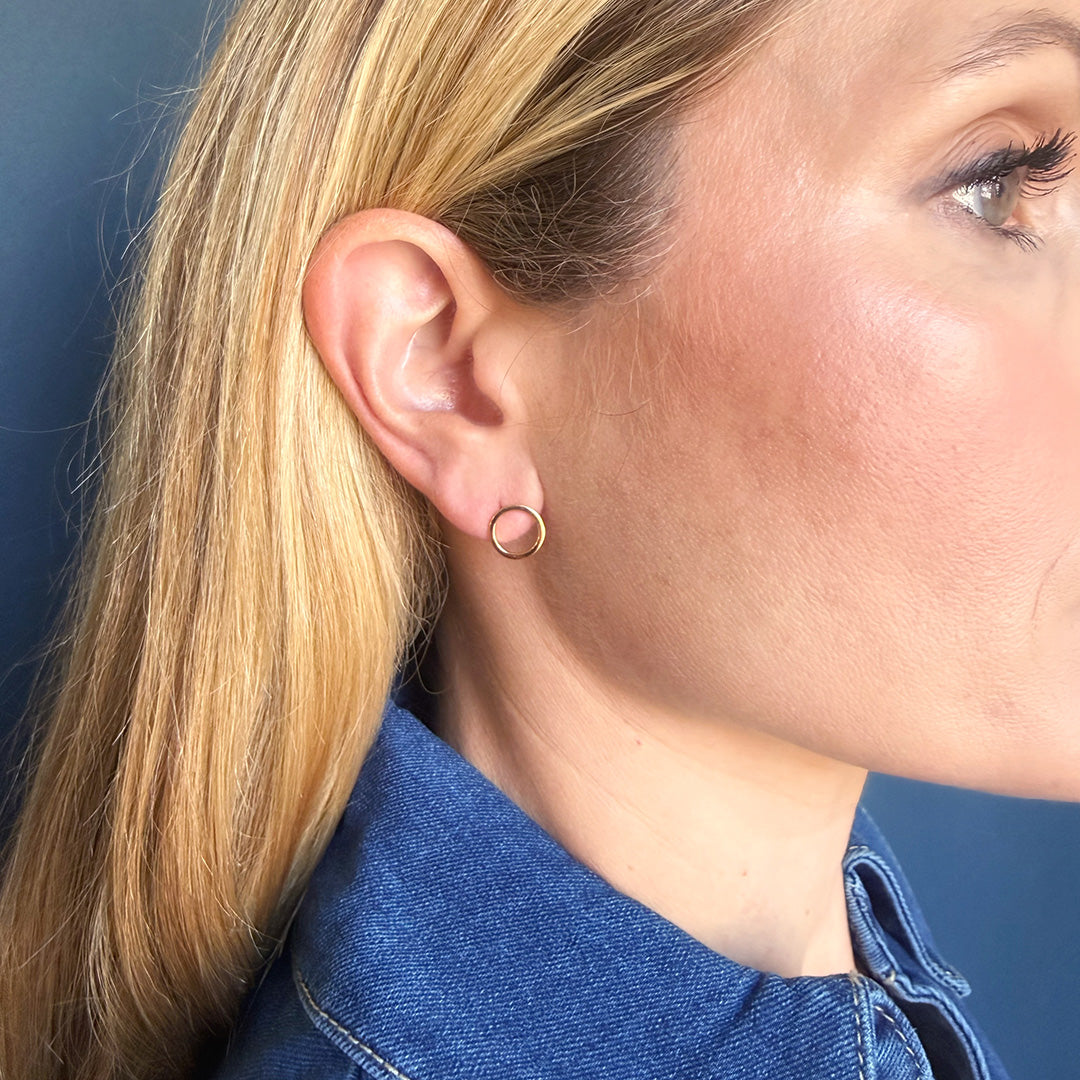 Close-up of a person wearing a gold circle stud with a blue denim shirt.