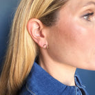 Close-up of a person wearing a gold circle stud with a blue denim shirt.