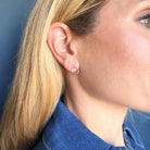 Close-up of a person wearing a silver circle stud with a blue denim shirt.