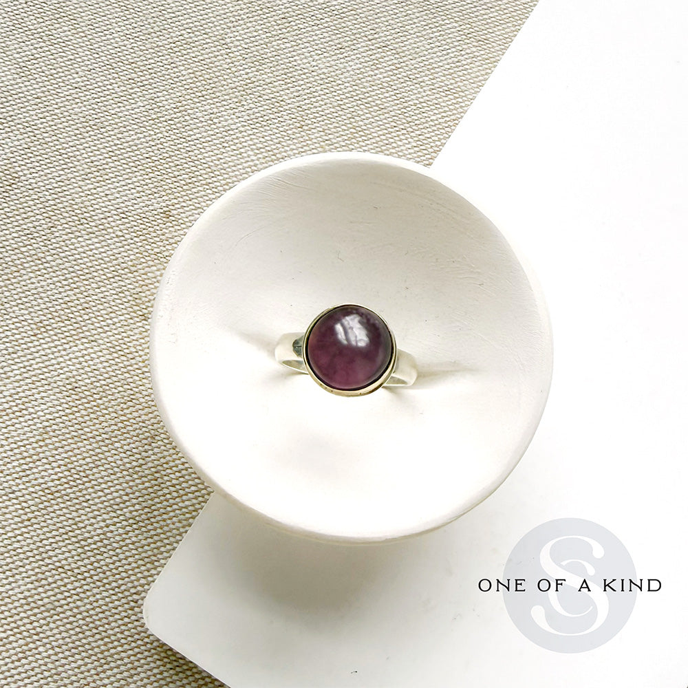 Round smooth cut mauve spinel ring in a white dish