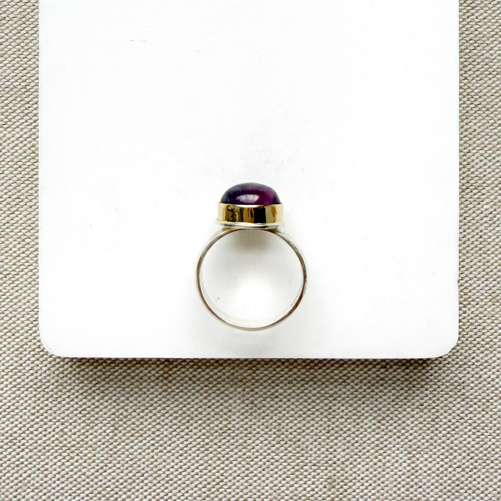 Side view of round smooth cut mauve spinel ring on a white dish